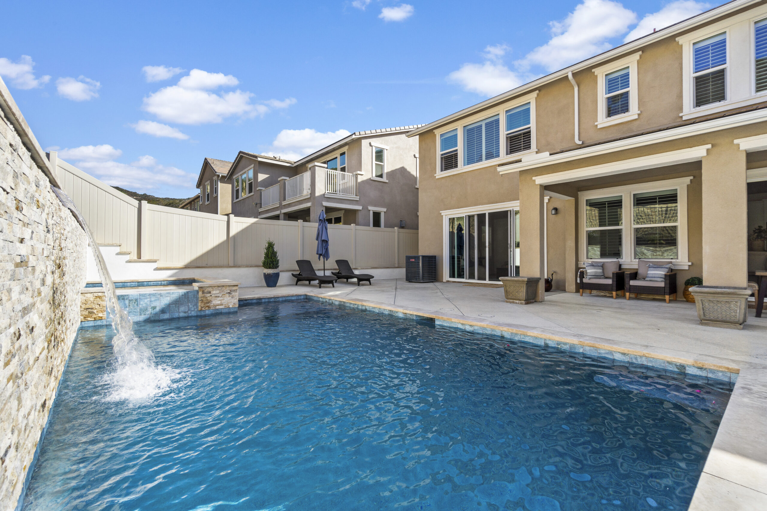 Luxury backyard pool with waterfall feature and seating area.