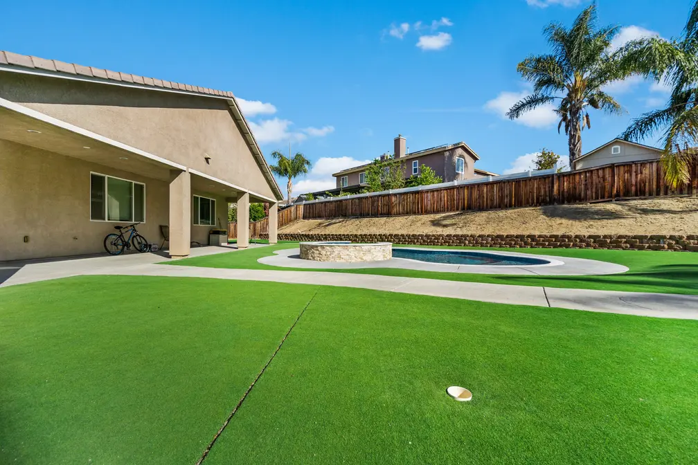 Backyard with artificial grass, a pool, and a fire pit under a clear sky.