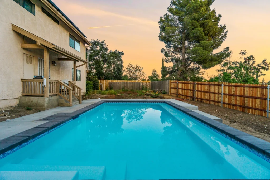 Backyard pool with a wooden deck at sunset.